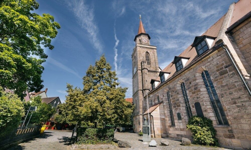 Historischer Kirchplatz mit steinerner Kirche und markantem Turm unter blauem Himmel