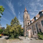 Historischer Kirchplatz mit steinerner Kirche und markantem Turm unter blauem Himmel