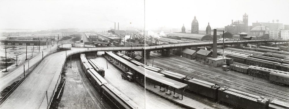 Historischer Bahnhof mit dichtem Gleisfeld, Zügen und Stadtbrücke